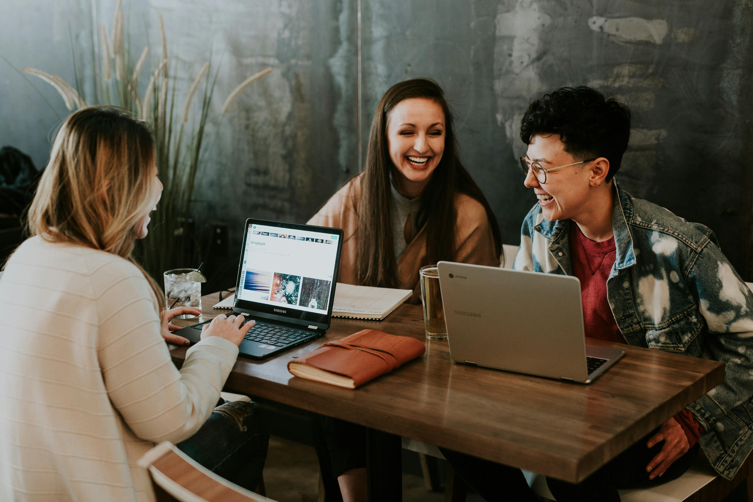 Three people at a table with computers and drinks, laughing.