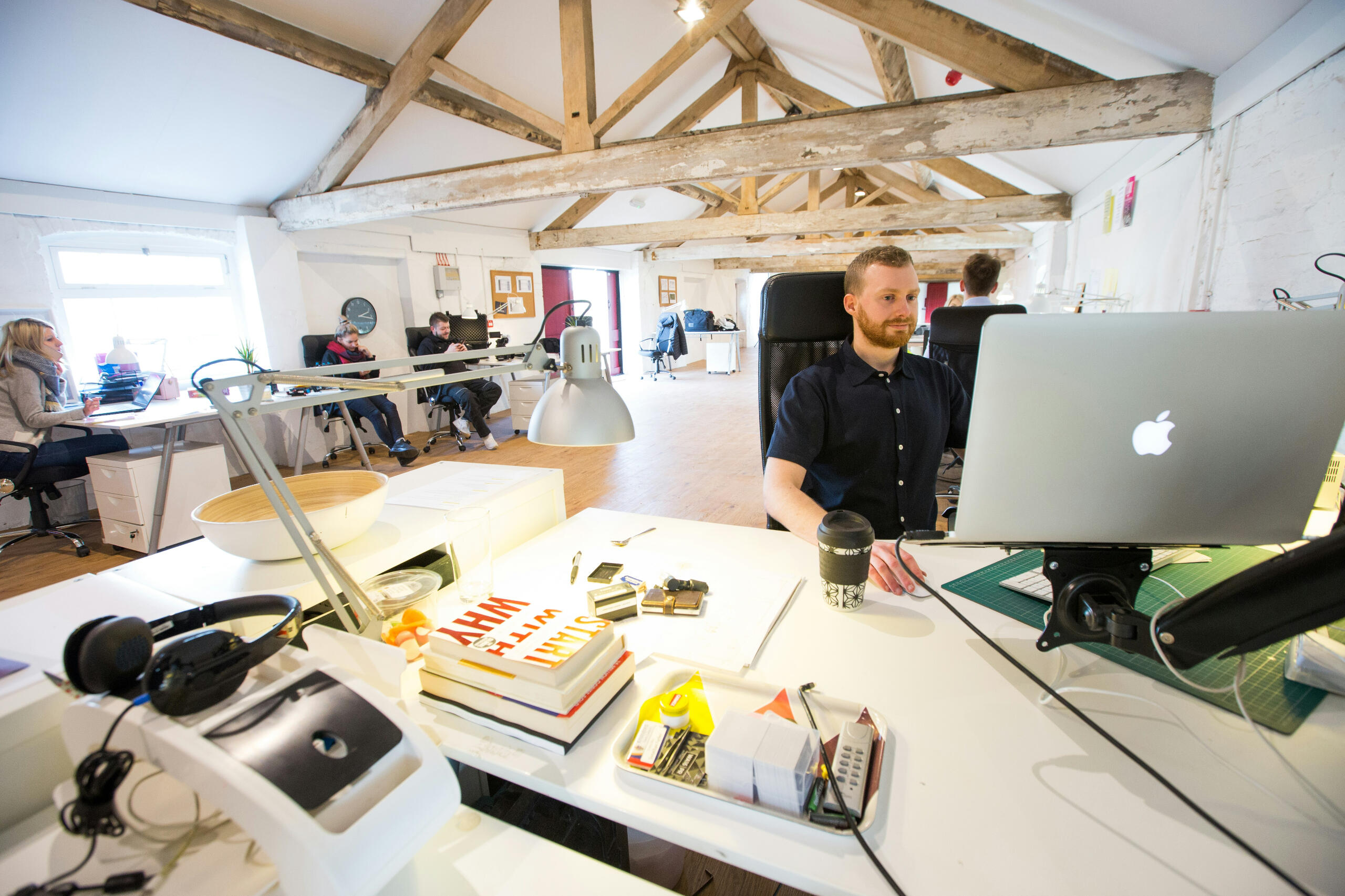 A man in a trendy, modern office with other employees, looking at his computer